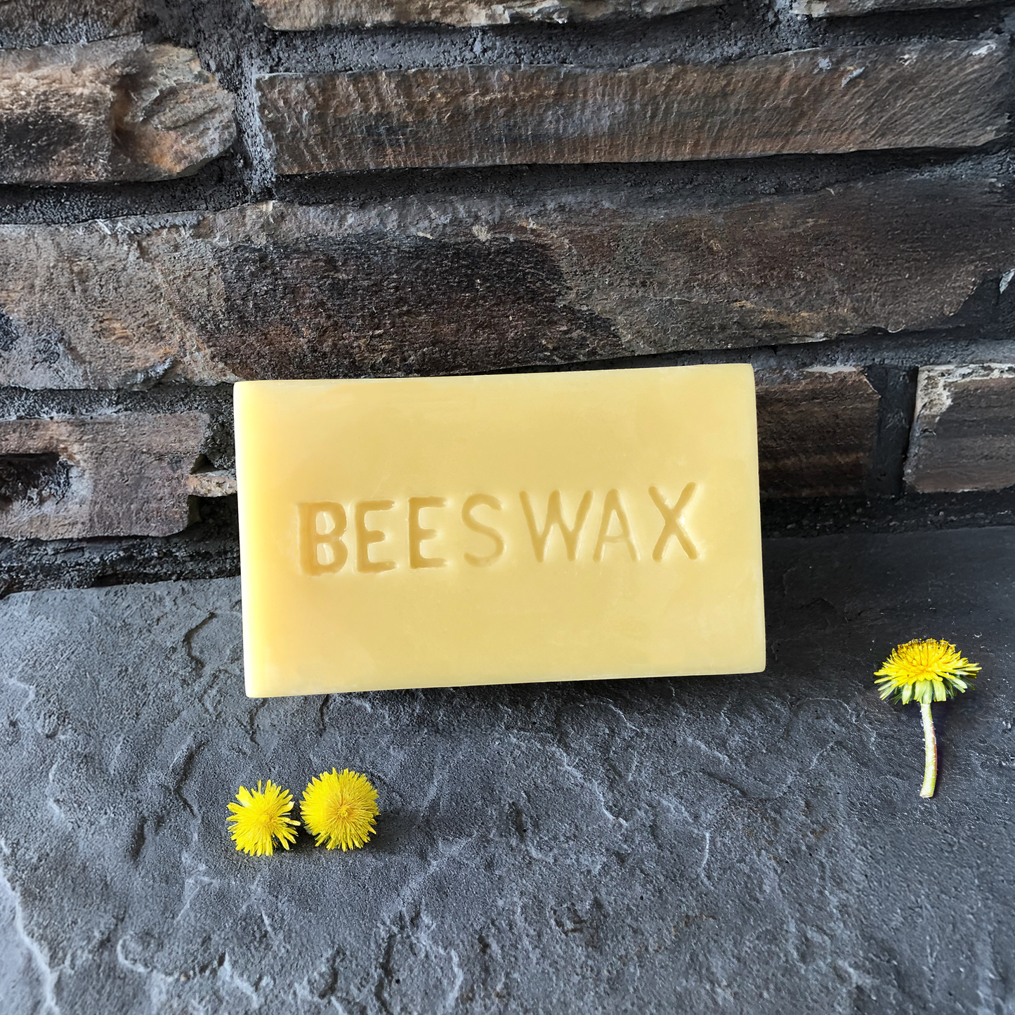 Bar of beeswax with dandelions on a stone surface