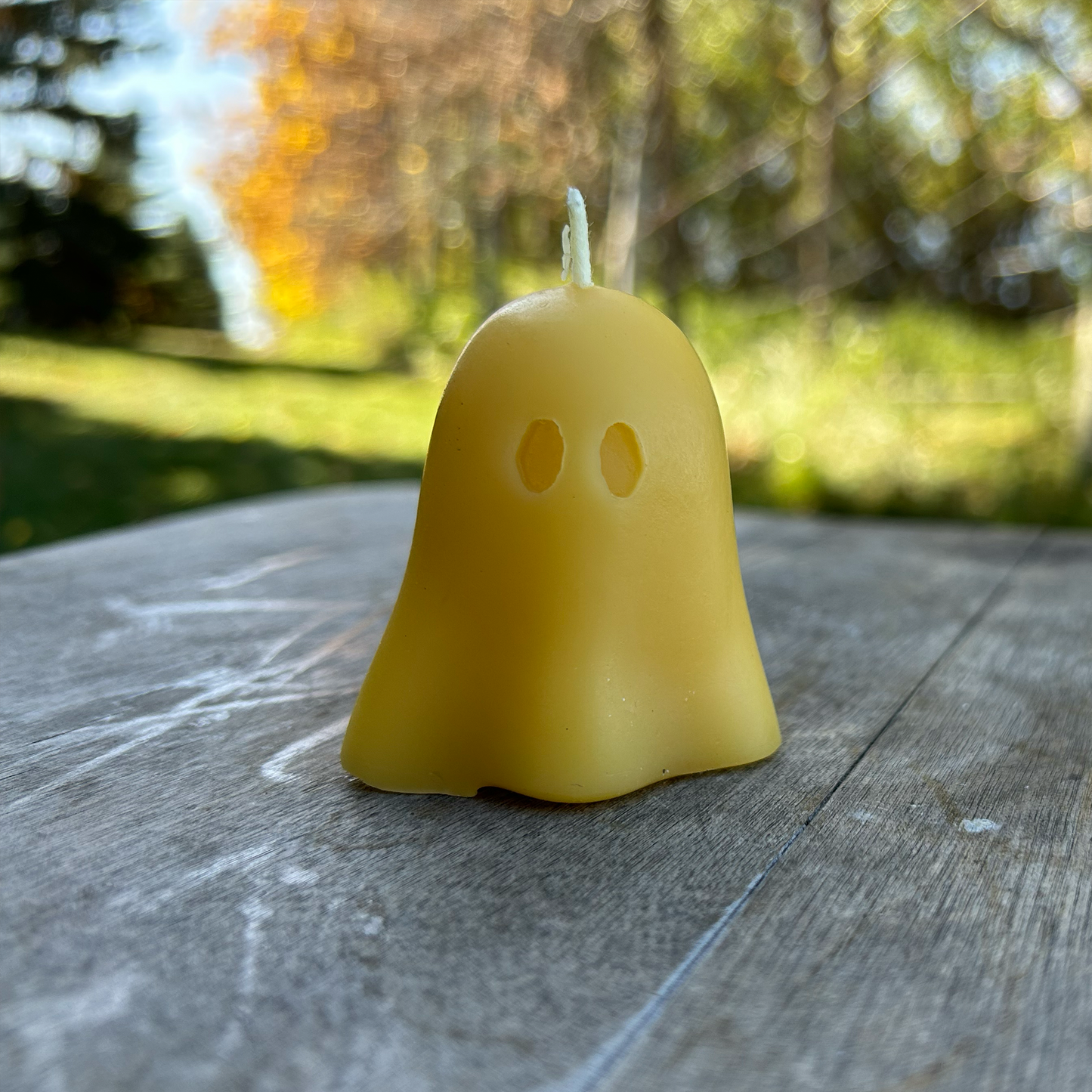 Yellow ghost-shaped beeswax candle on a wooden surface with a blurred natural background