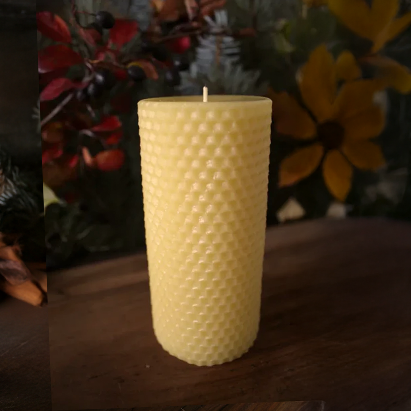 Beeswax candle with honeycomb pattern on a wooden surface with decorative plants in the background