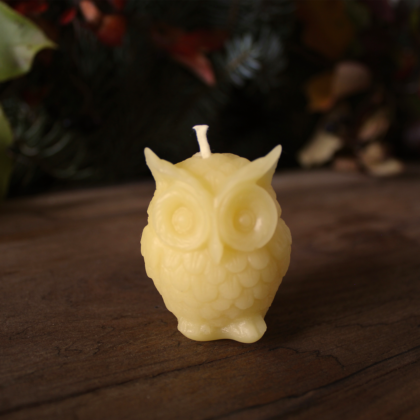 Owl-shaped beeswax candle on a wooden surface with a blurred natural background
