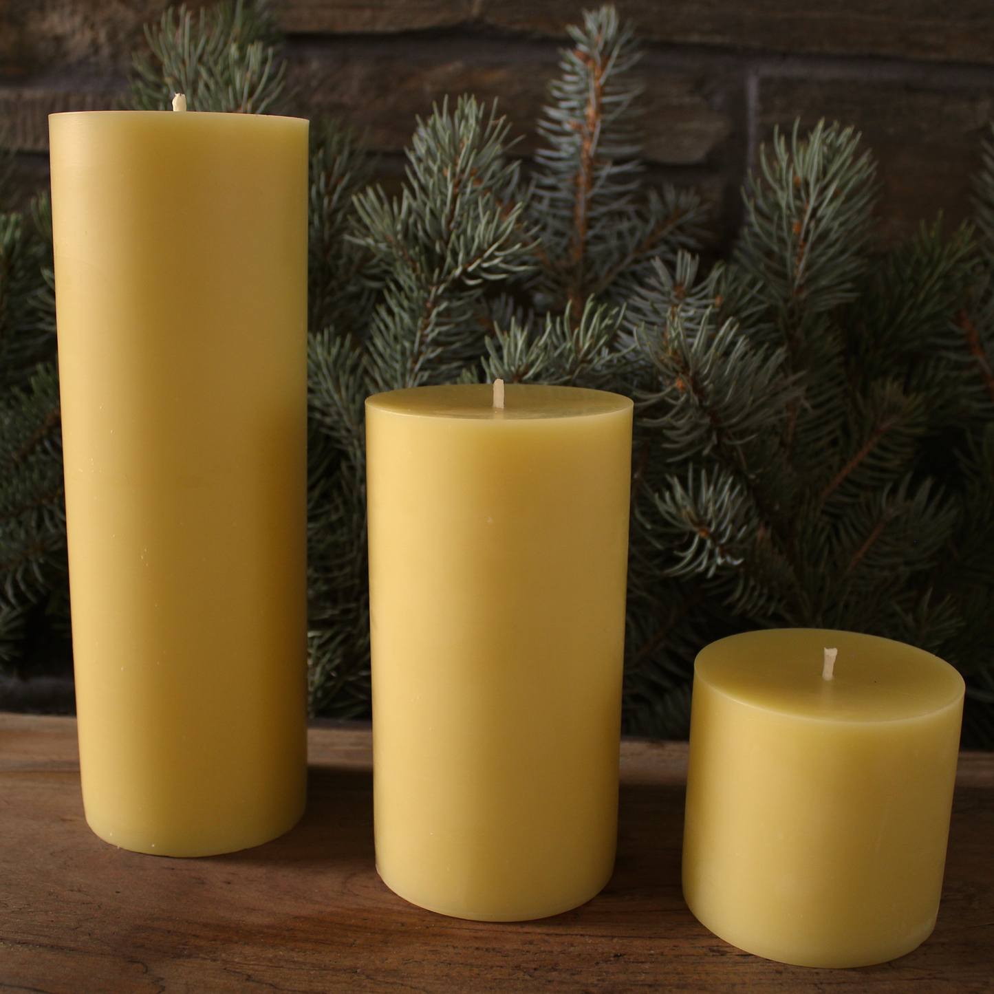 Three yellow beeswax candles of different sizes on a wooden surface with a dark background