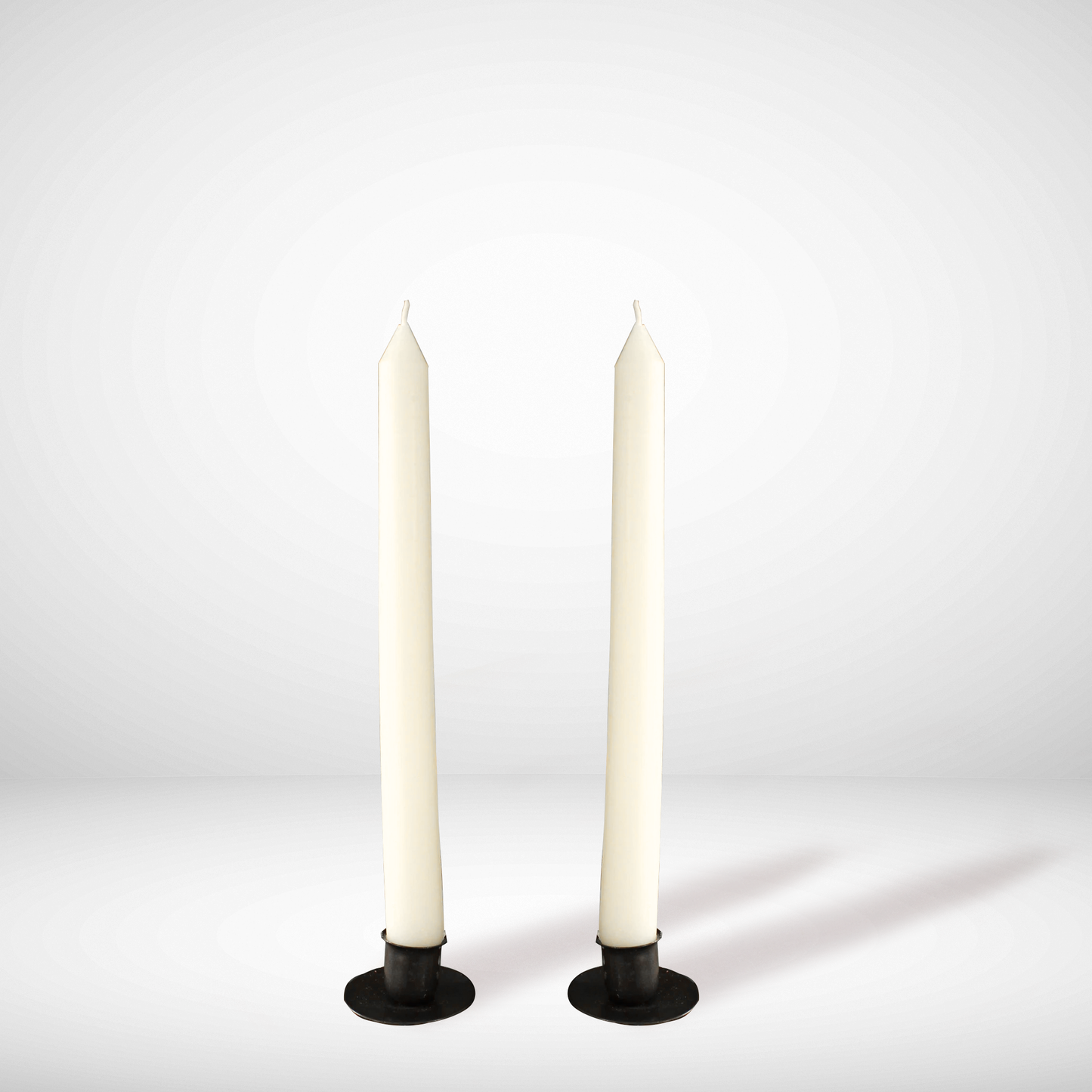 Two white beeswax candles on black holders against a light gray background