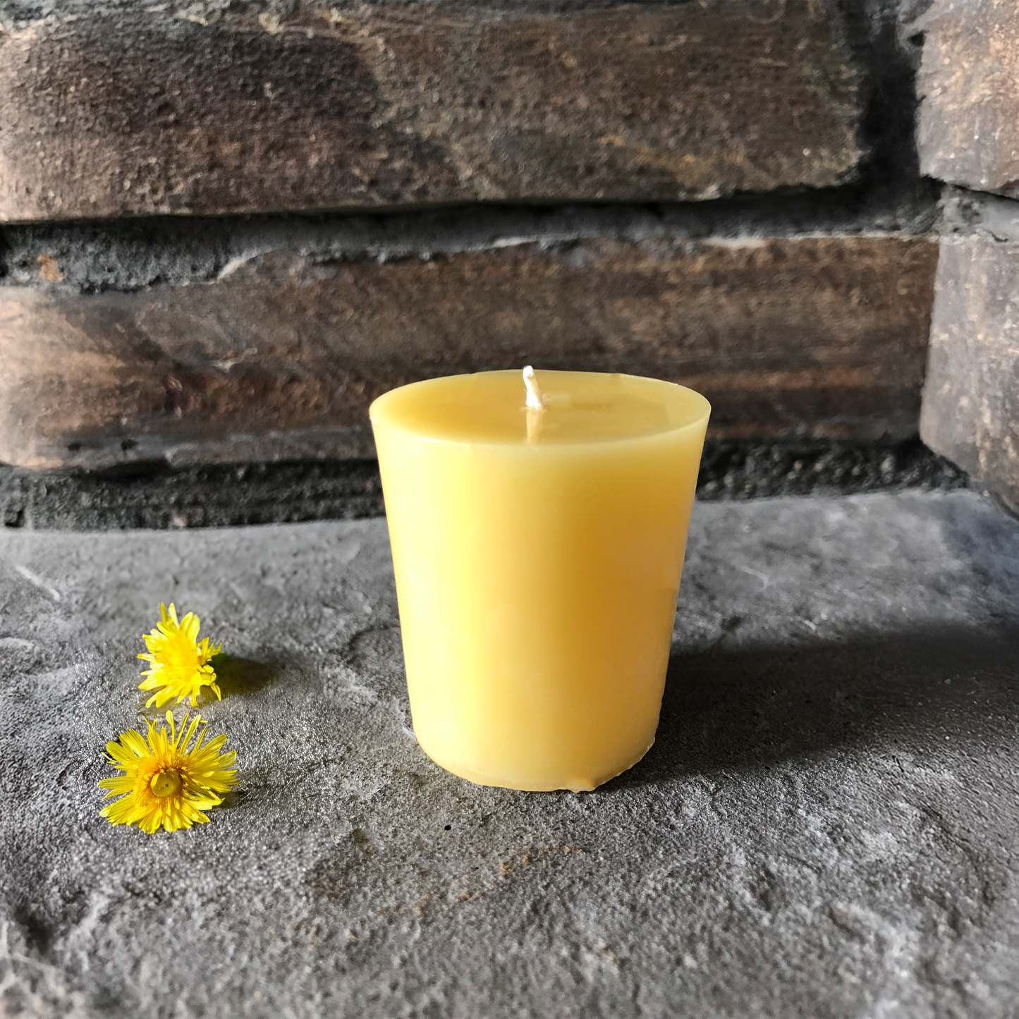 Yellow candle and two yellow flowers on a stone surface with a stone wall background