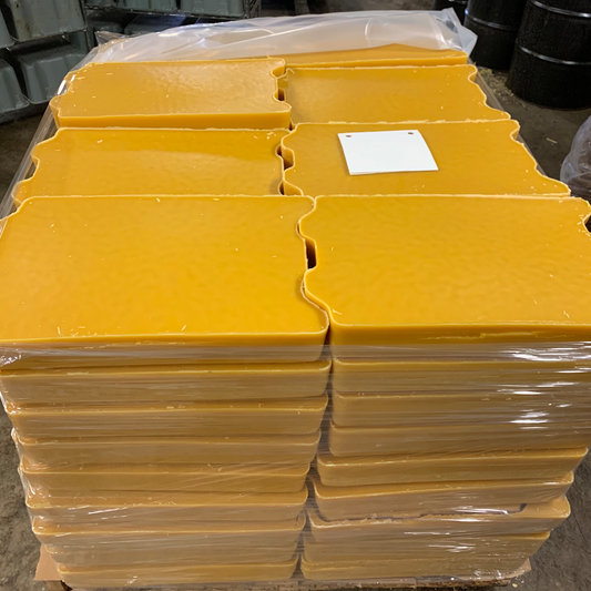 Stack of yellow beeswax blocks with a white label on a concrete floor.