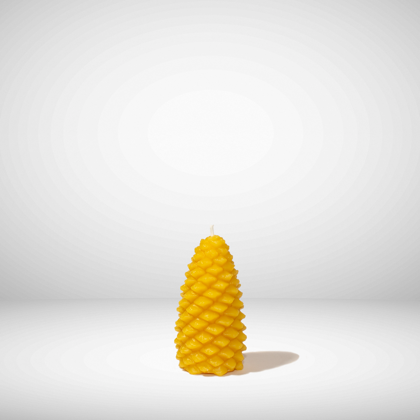 A yellow beeswax candle shaped like a pinecone, set against a neutral background
