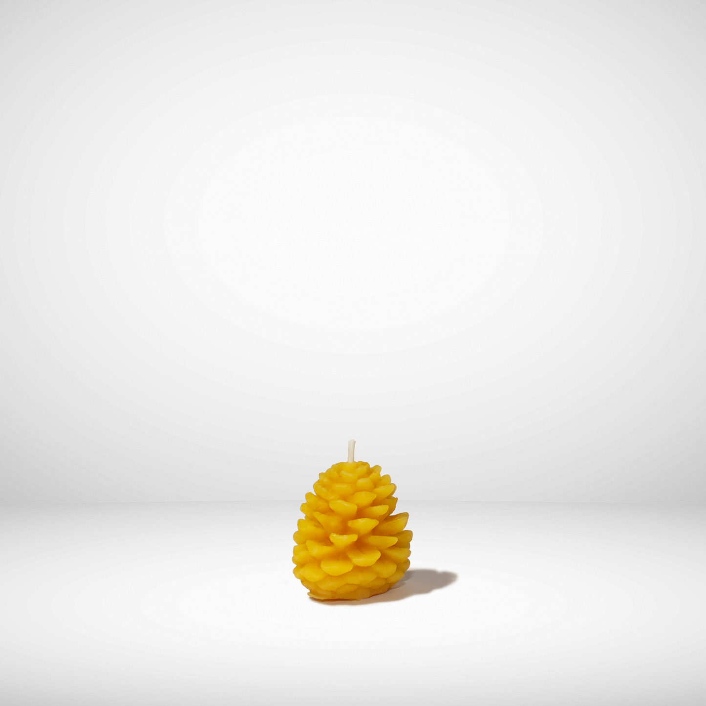 A yellow beeswax candle shaped like a pinecone, set against a neutral background