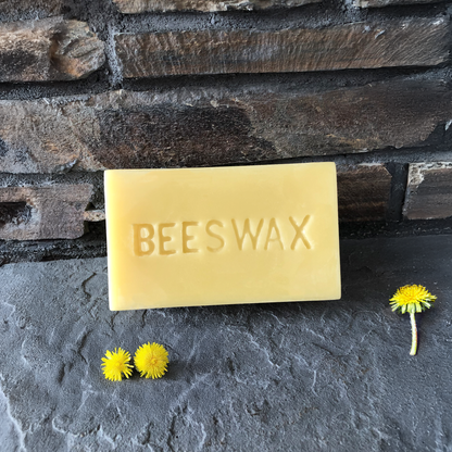 Bar of beeswax with dandelions on a stone surface