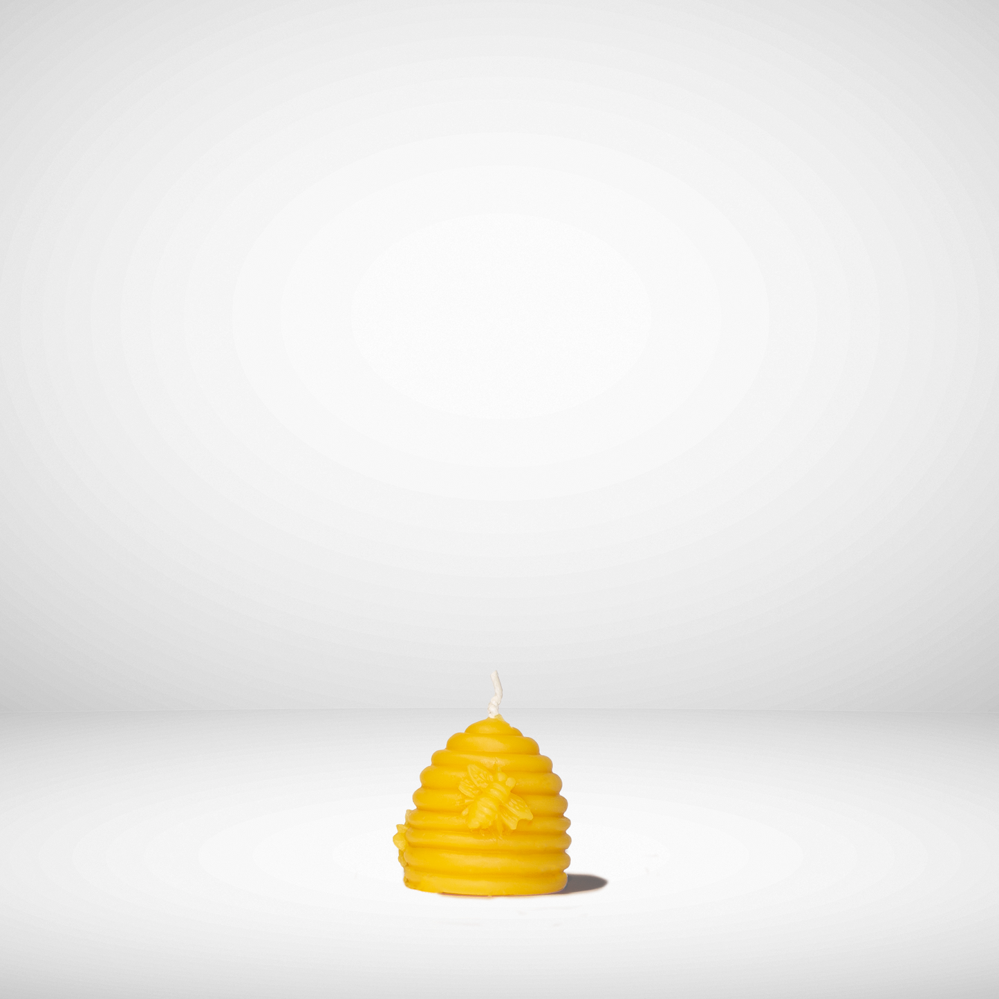 A yellow beeswax candle shaped like a beehive, set against a plain background.