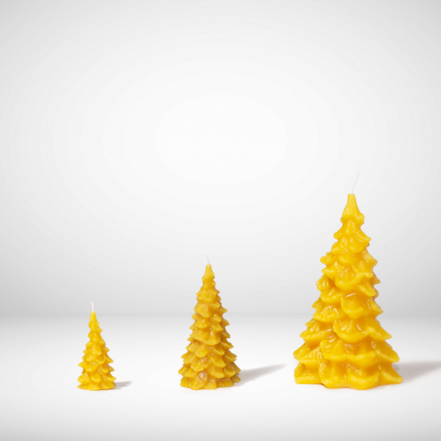 Three yellow Christmas tree-shaped beeswax candles on a white background