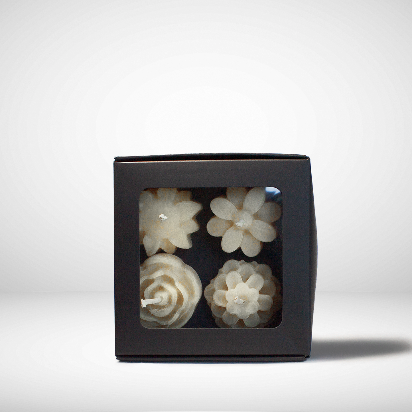 Black box with four decorative white beeswax candles pieces inside on a white background