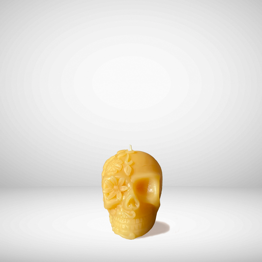A yellow beeswax candle in the shape of a skull with floral patterns.