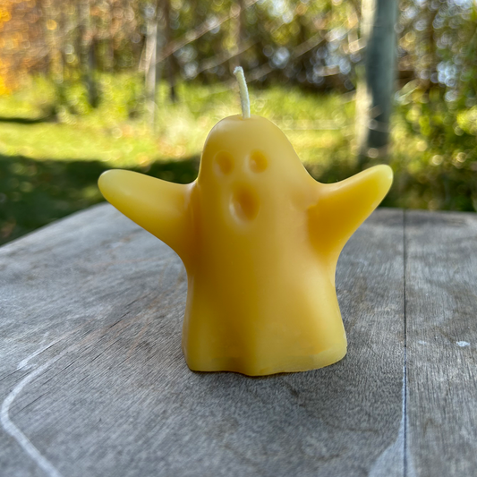 Yellow beeswax ghost-shaped candle on a wooden surface with a blurred natural background