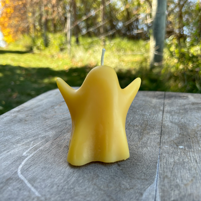 Yellow beeswax candle shaped like a ghost on a wooden surface with a natural background