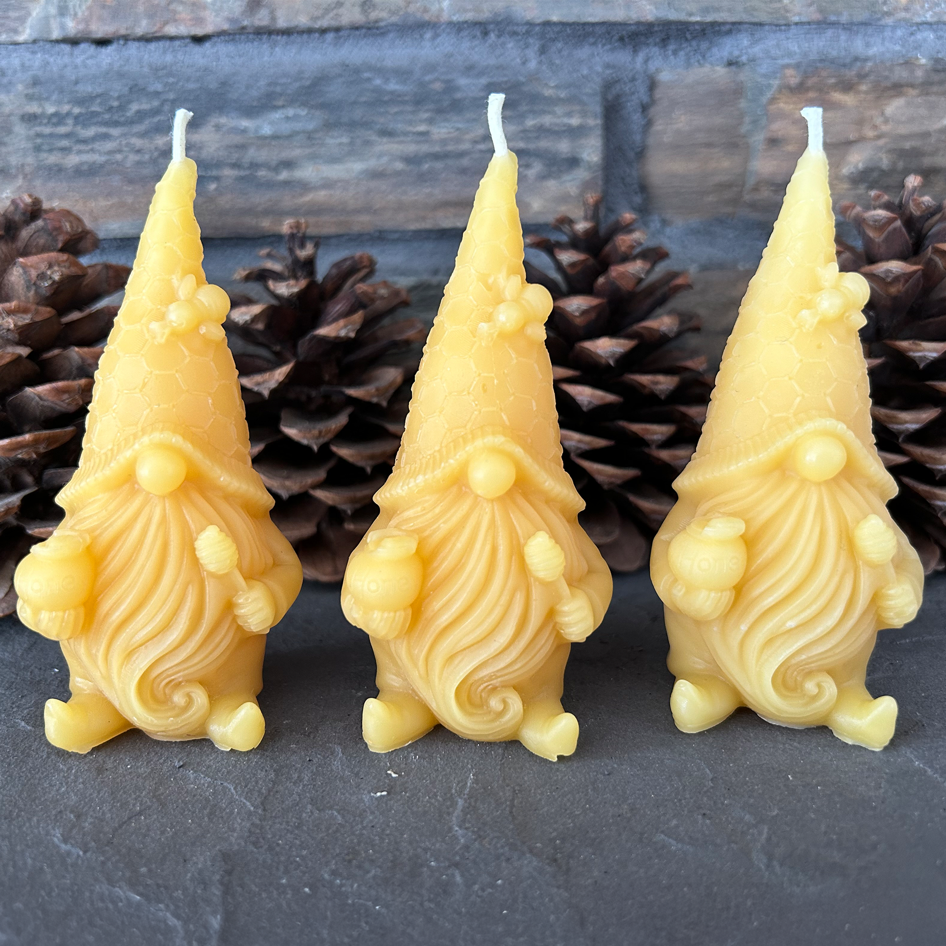 Three yellow gnome-shaped candles with pinecones in the background on a dark surface