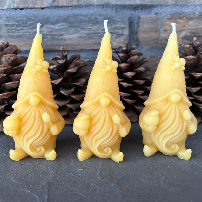 Three yellow gnome-shaped candles with pinecones in the background on a dark surface