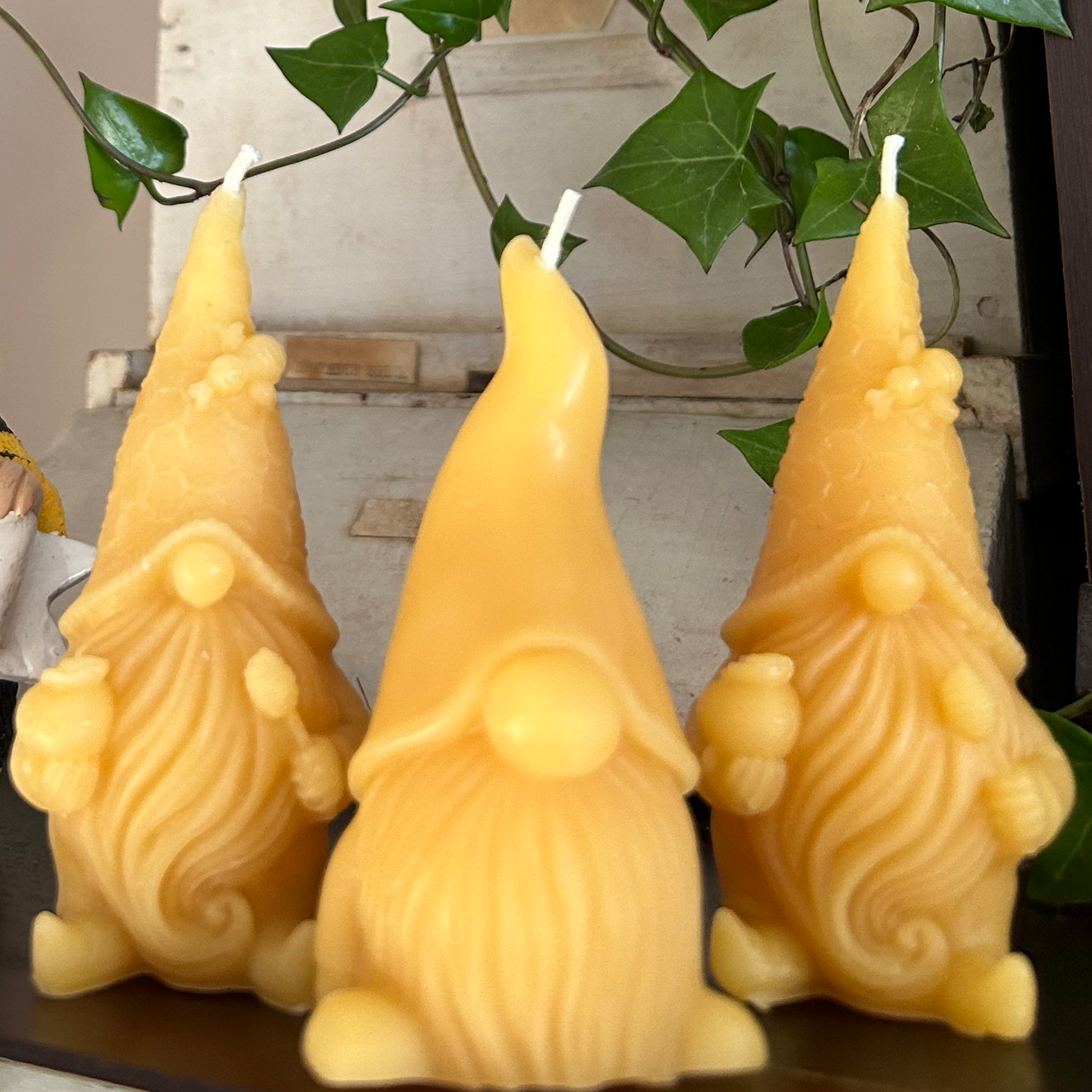 Three gnome-shaped beeswax candles on a surface with green leaves in the background