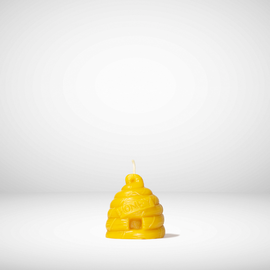 A beehive-shaped beeswax candle in yellow color with a visible warm glow, against a white background