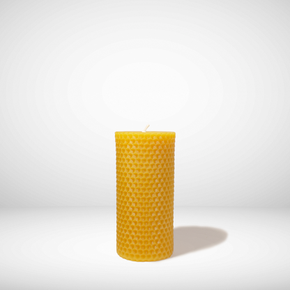 A yellow beeswax pillar candle with a honeycomb texture, standing upright against a white background.