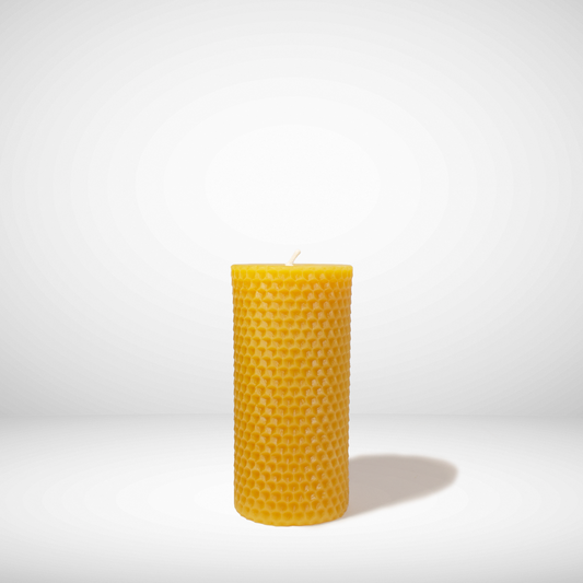 A yellow beeswax pillar candle with a honeycomb texture, standing upright against a white background.