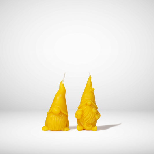 Two yellow beeswax candles molded in the shape of gnomes, set against a neutral background.
