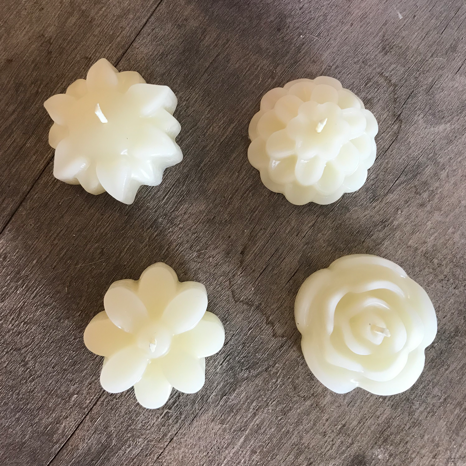Four white floral-shaped beeswax candles on a wooden surface