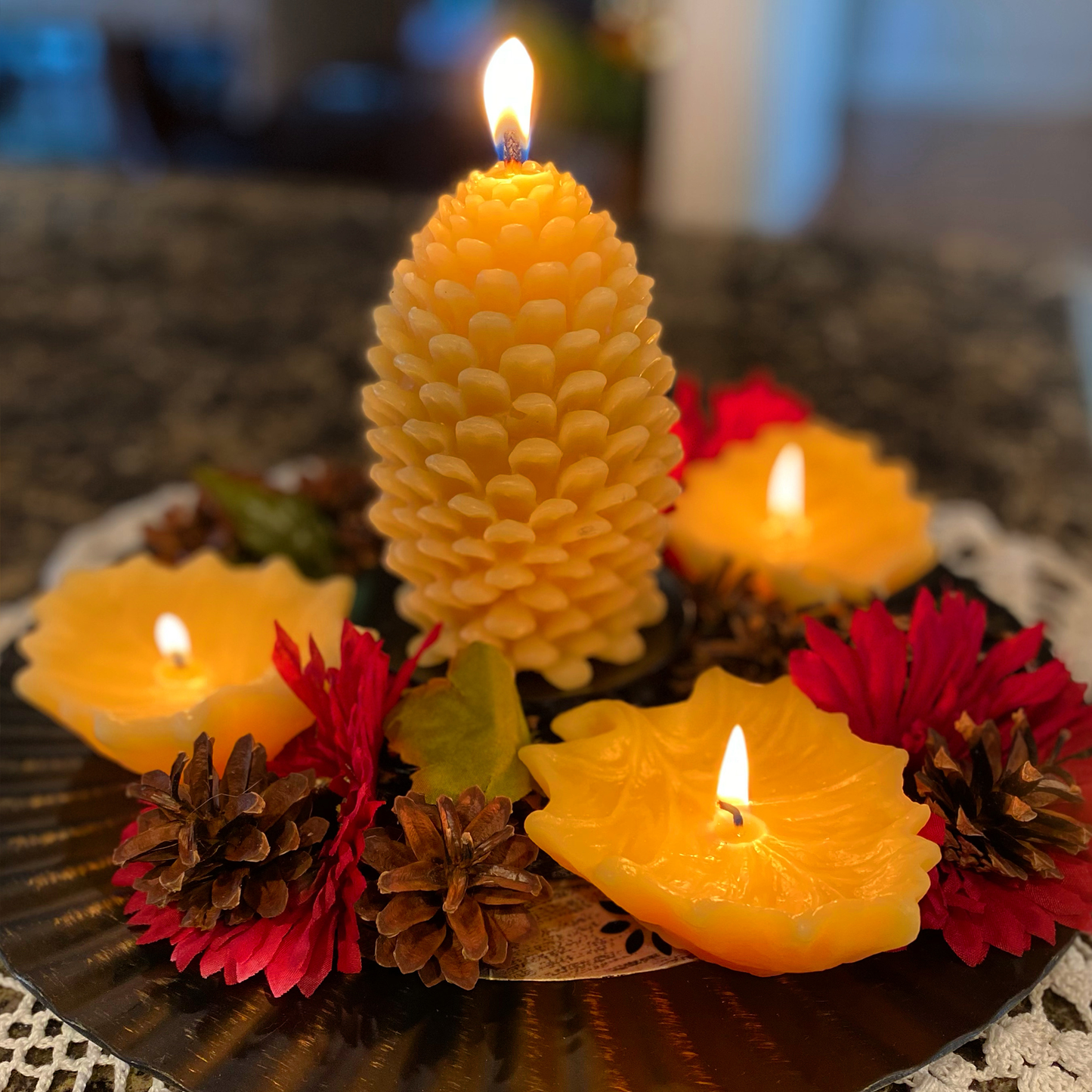 Decorative beeswax candles with a pine cone-shaped beeswax candle and floral elements on a textured surface.
