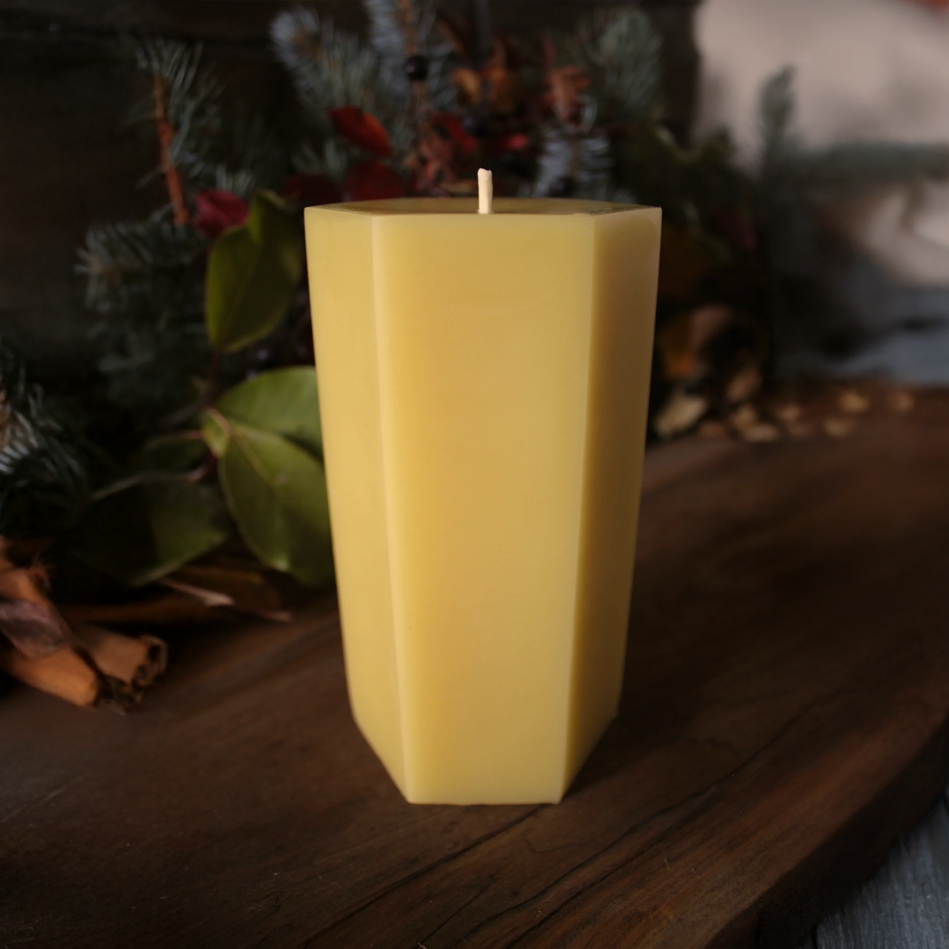 Yellow candle on a wooden surface with greenery in the background