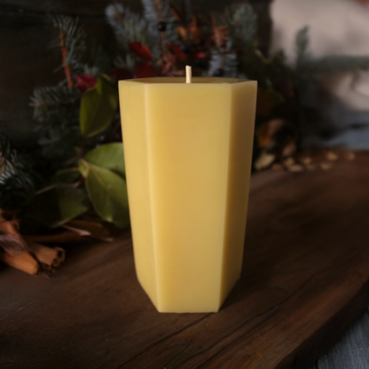 Yellow candle on a wooden surface with greenery in the background