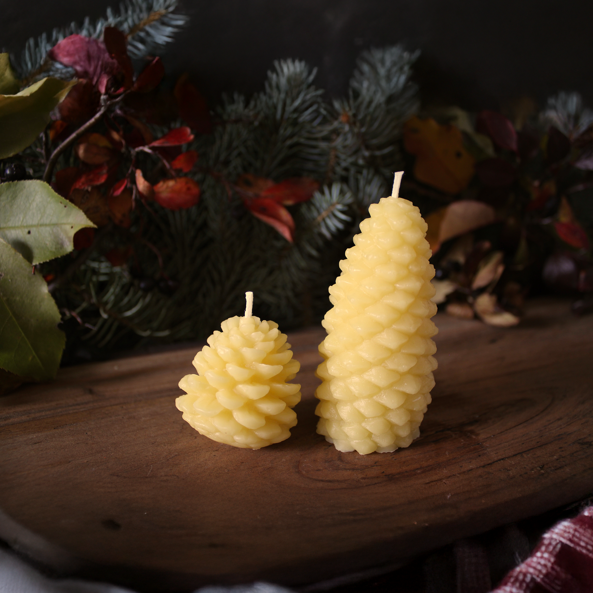 Two pine cone-shaped beeswax candles on a wooden surface with a decorative background.