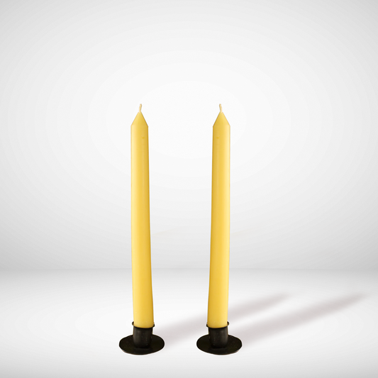 Two yellow beeswax taper candles standing upright on a round, dark base against a white background.