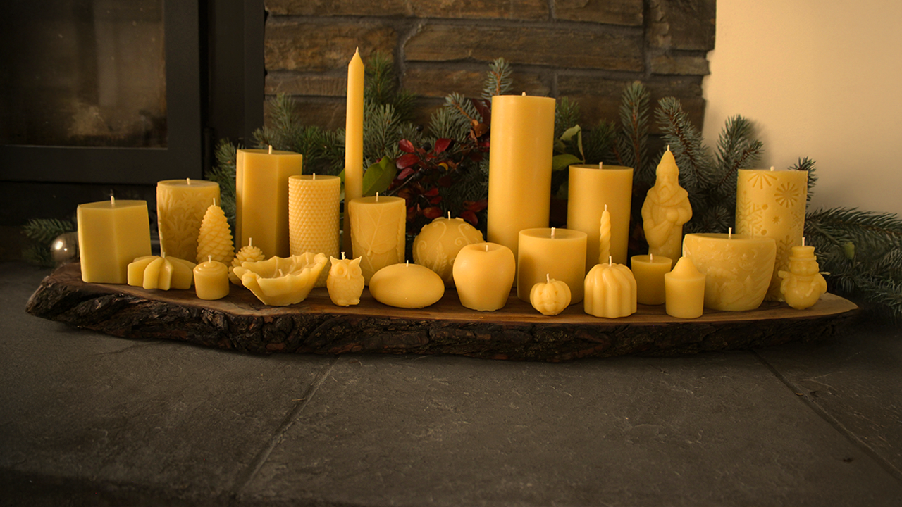 Assorted yellow candles on a wooden tray with a fireplace and greenery in the background