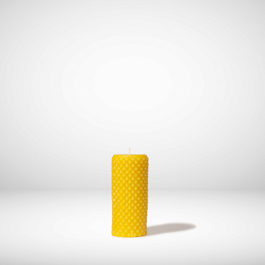 A yellow beeswax pillar candle with a diamond pattern, standing upright against a white background.