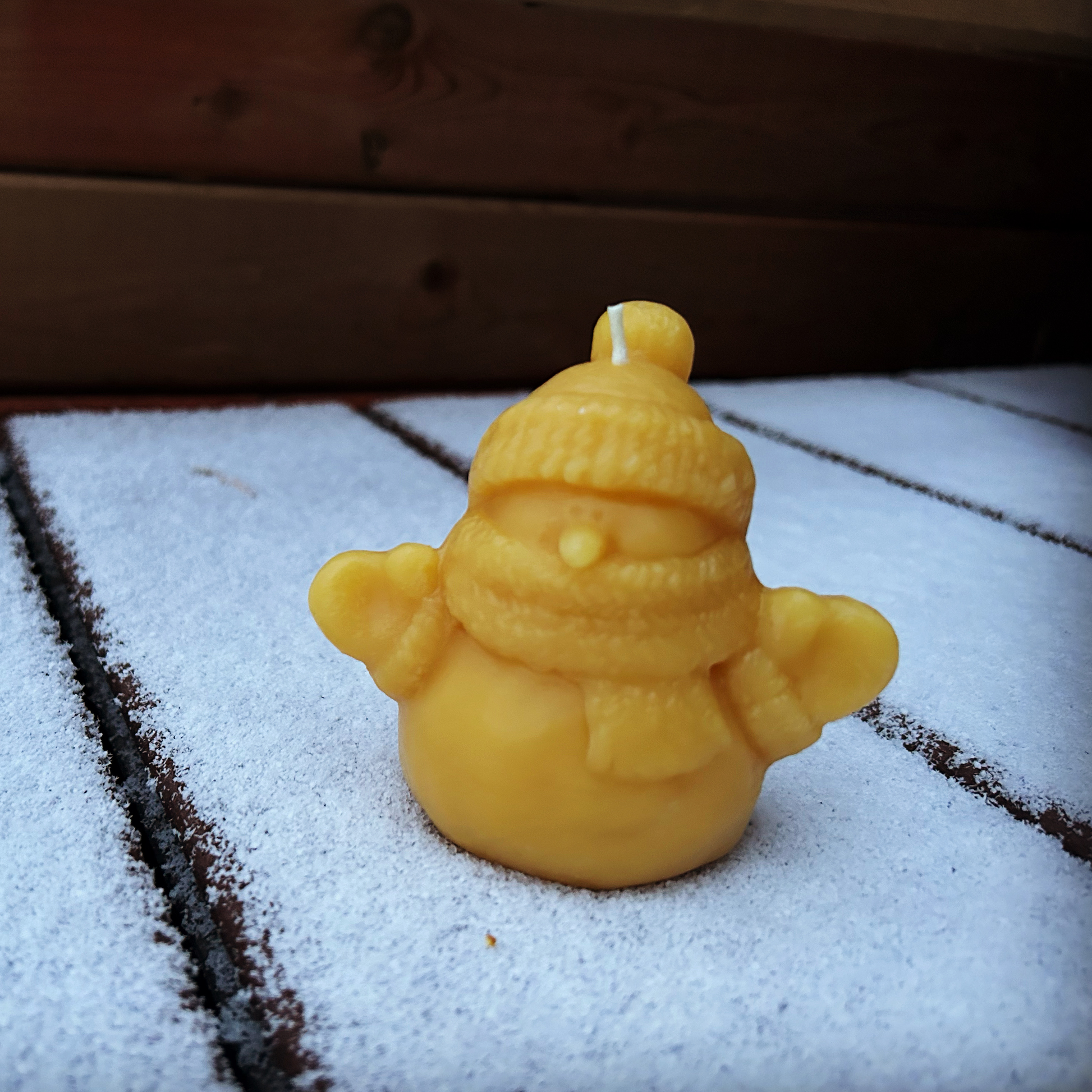 Yellow snowman-shaped beeswax candle on a snowy surface