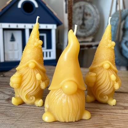 Three yellow gnome-shaped beeswax candles on a wooden surface with a decorative house in the background.