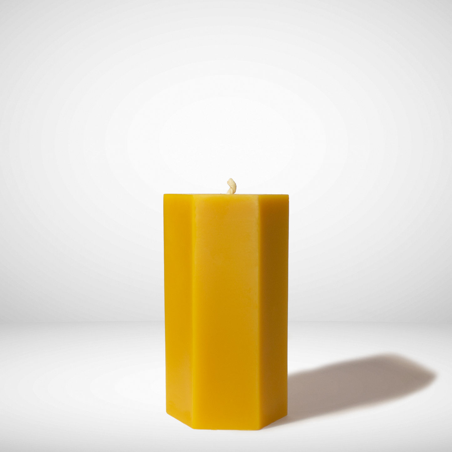 A single yellow hexagon beeswax pillar candle against a white background.