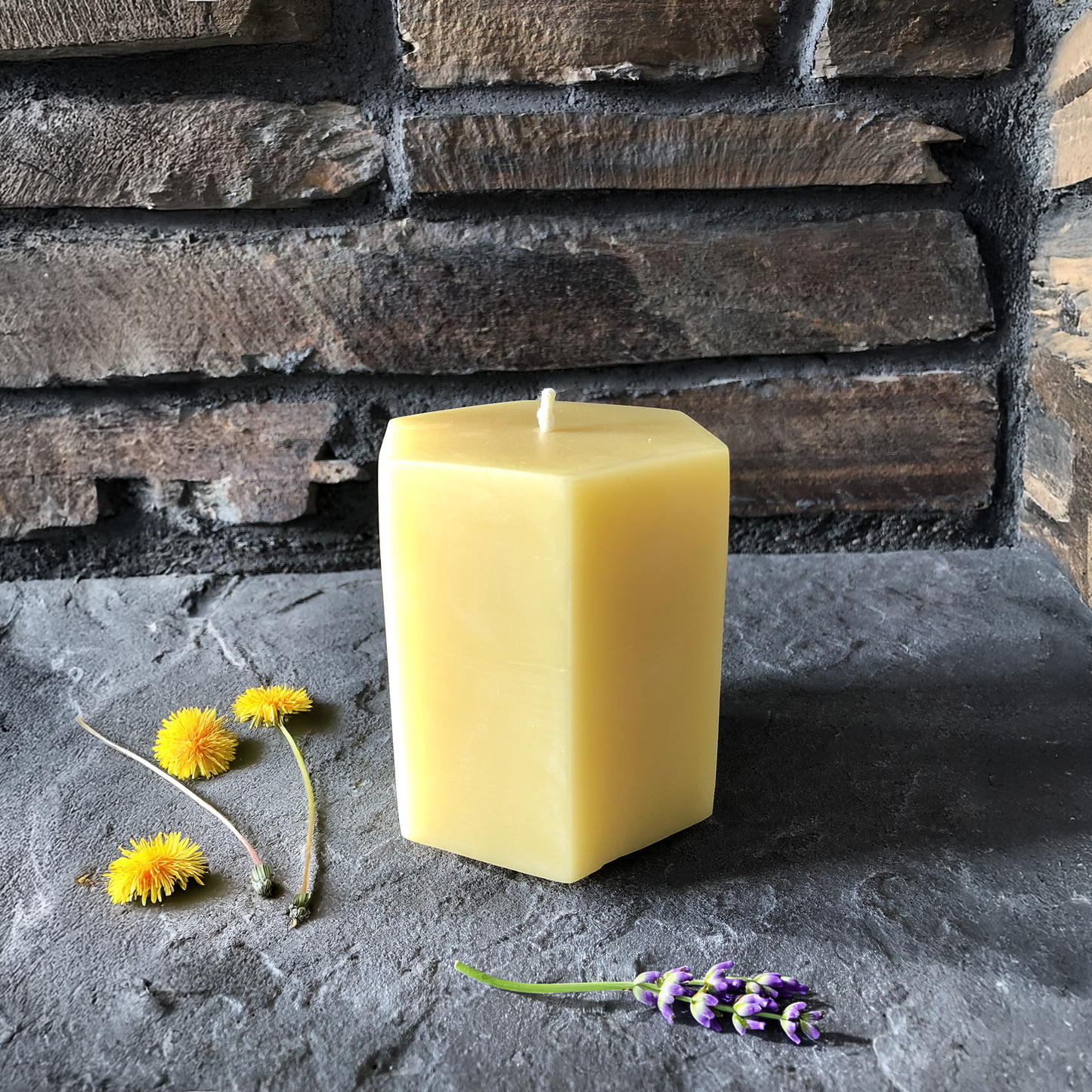 Hexagonal beeswax candle on a stone surface with flowers