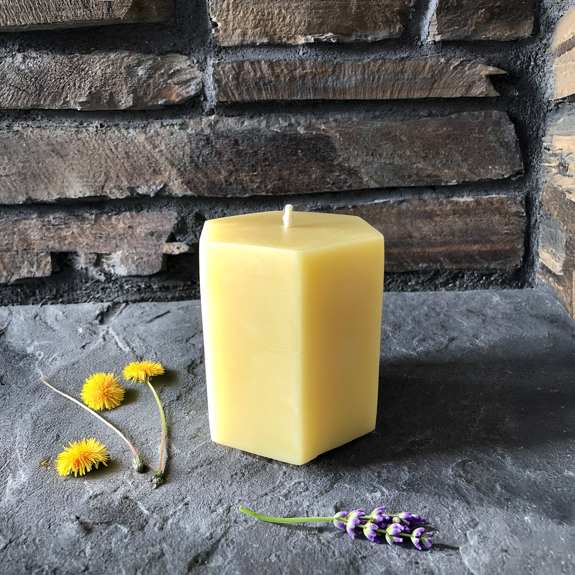 Hexagonal beeswax candle on a stone surface with flowers