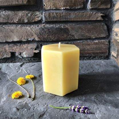 Hexagonal beeswax candle on a stone surface with flowers
