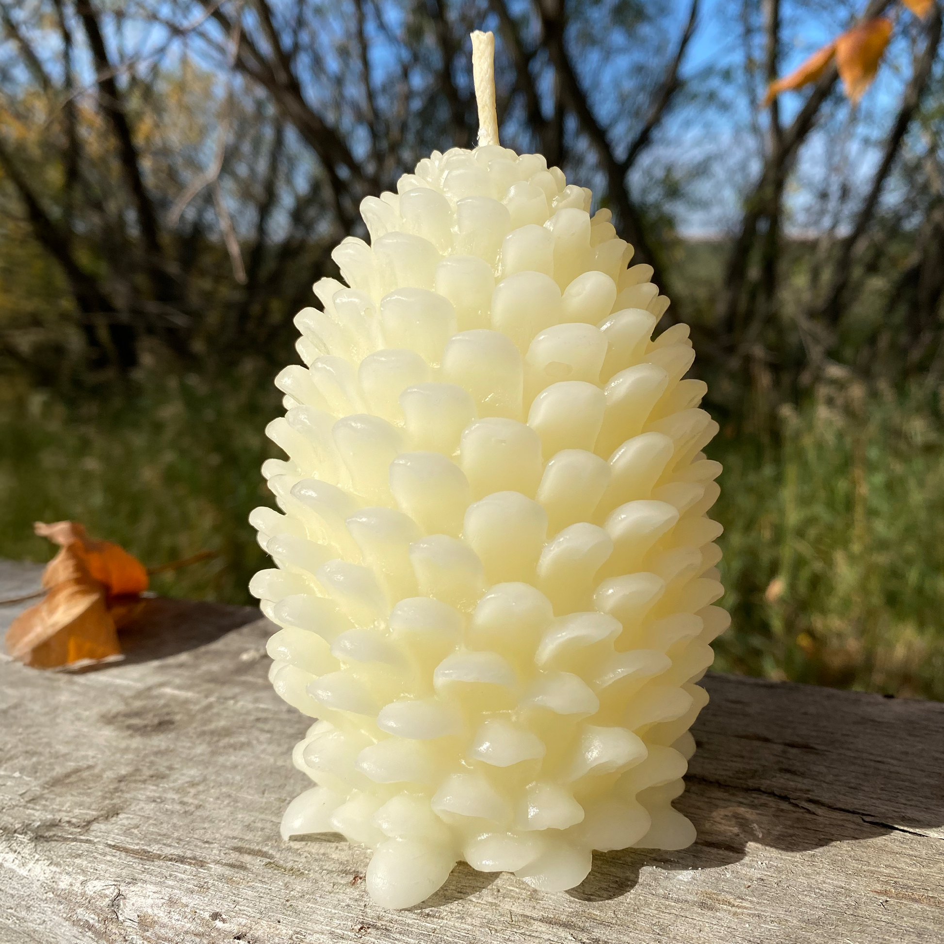 Pine cone-shaped beeswax candle on a wooden surface with a natural background