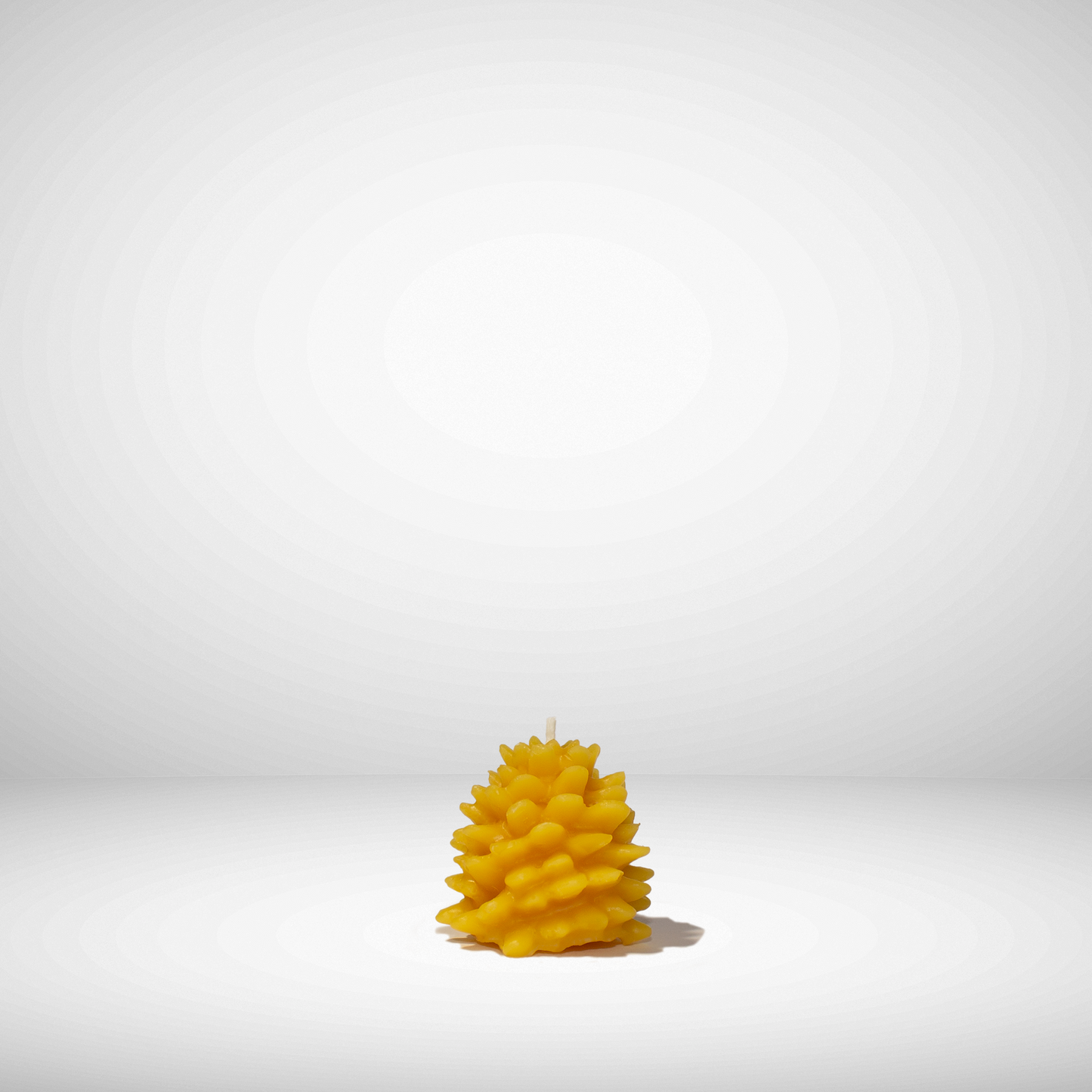 A yellow beeswax candle shaped like a pinecone, set against a neutral background