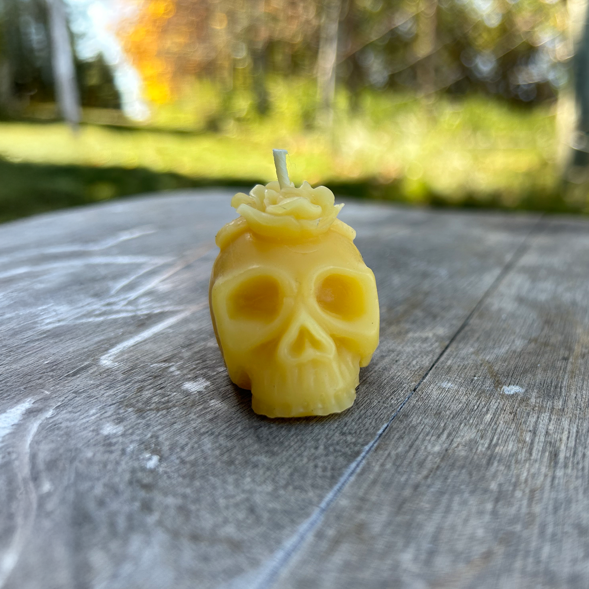 Yellow skull-shaped candle on a wooden surface with a blurred natural background