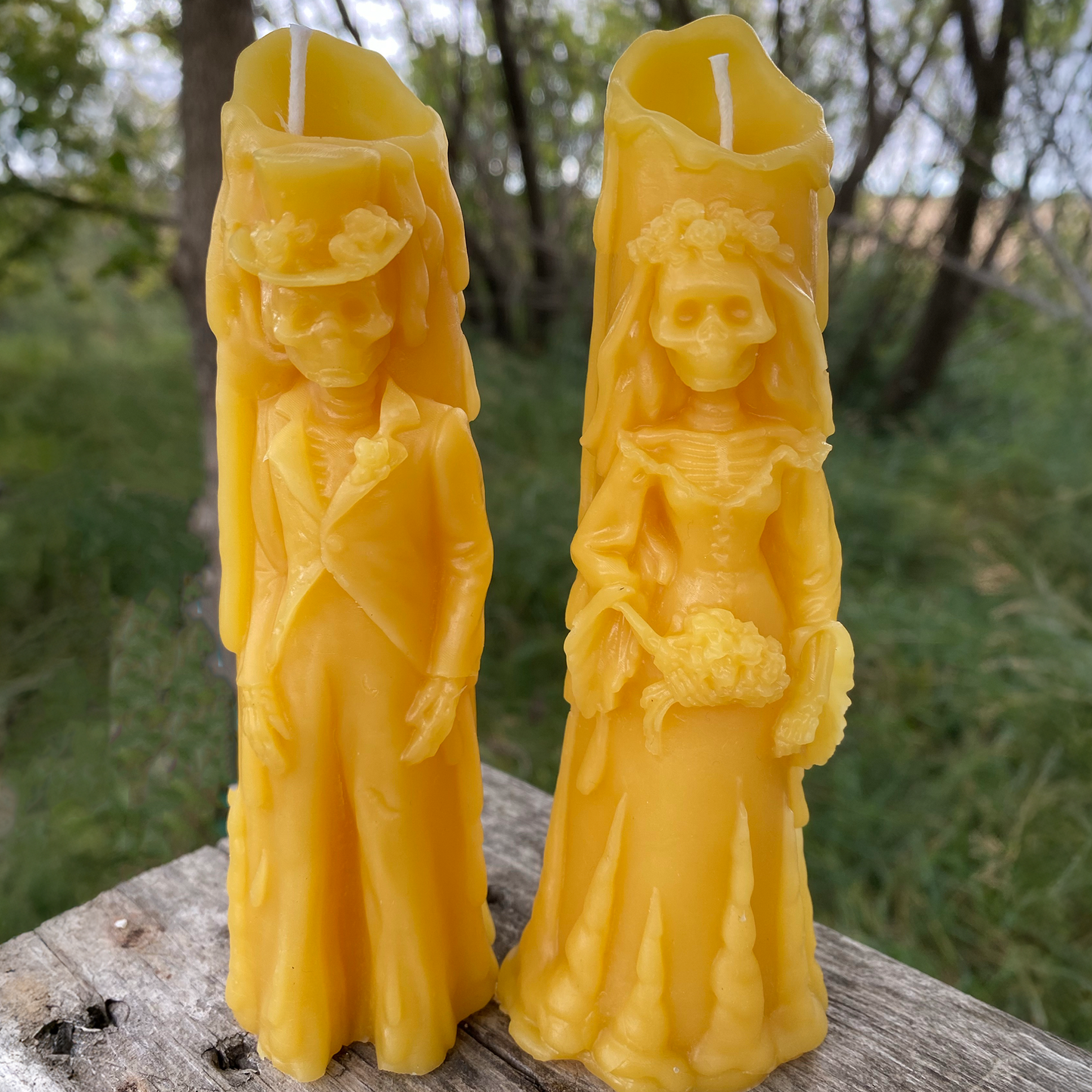 Two yellow beeswax candles shaped like people on a wooden surface with a natural background.