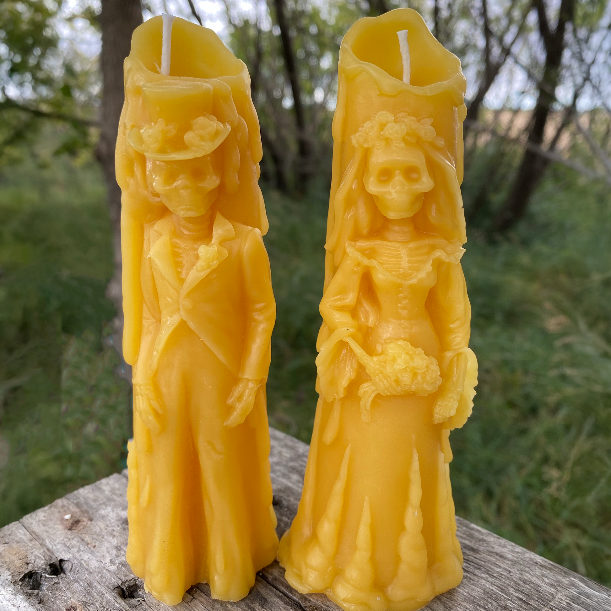 Two yellow beeswax candles shaped like people on a wooden surface with a natural background.