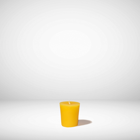 A single yellow beeswax votive candle on a white background.