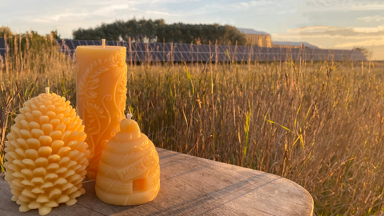 Three honeycomb-patterned beeswax candles on a wooden surface with a scenic background of a field and mountains.