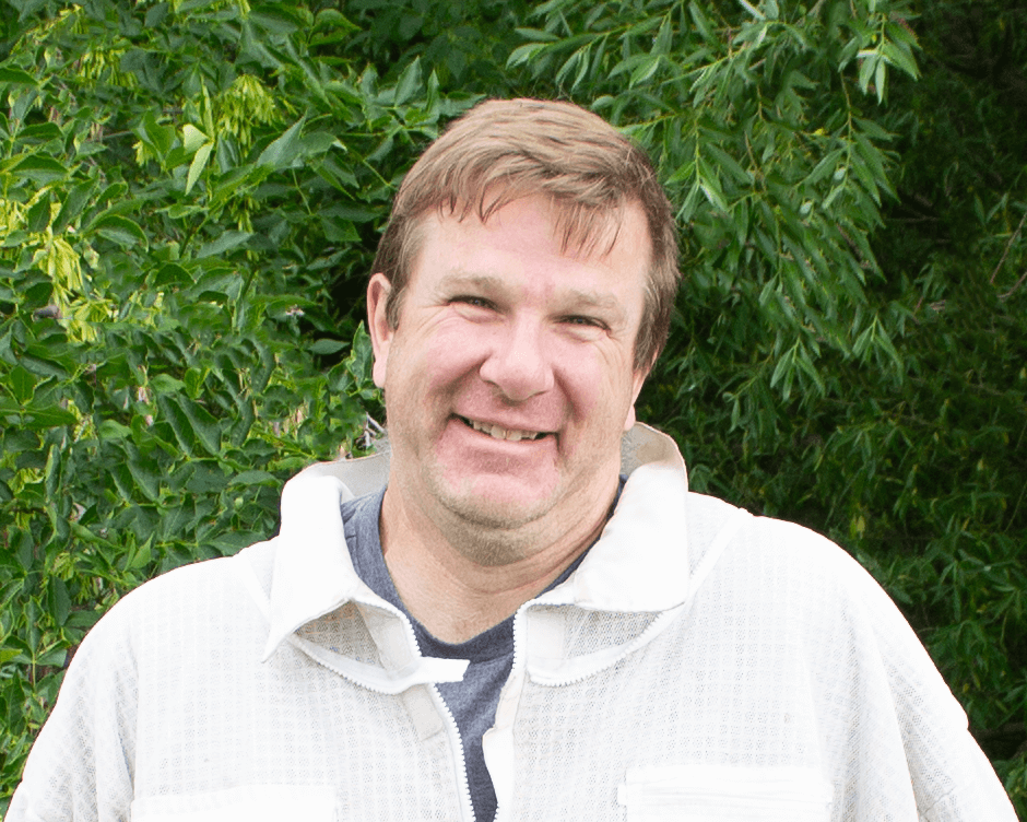 Man wearing a light-colored shirt with a green leafy background
